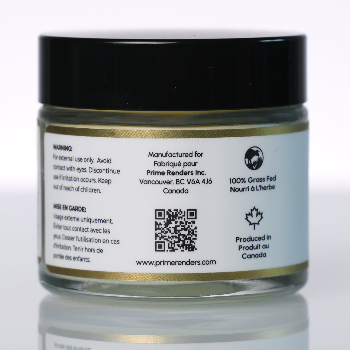 A small clear cosmetic jar with a black lid and a white printed label, photographed on a light gray reflective studio surface. The label includes text and a QR code for Prime Renders beef tallow balm