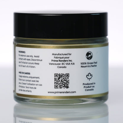 A small clear cosmetic jar with a black lid and a white printed label, photographed on a light gray reflective studio surface. The label includes text and a QR code for Prime Renders beef tallow balm