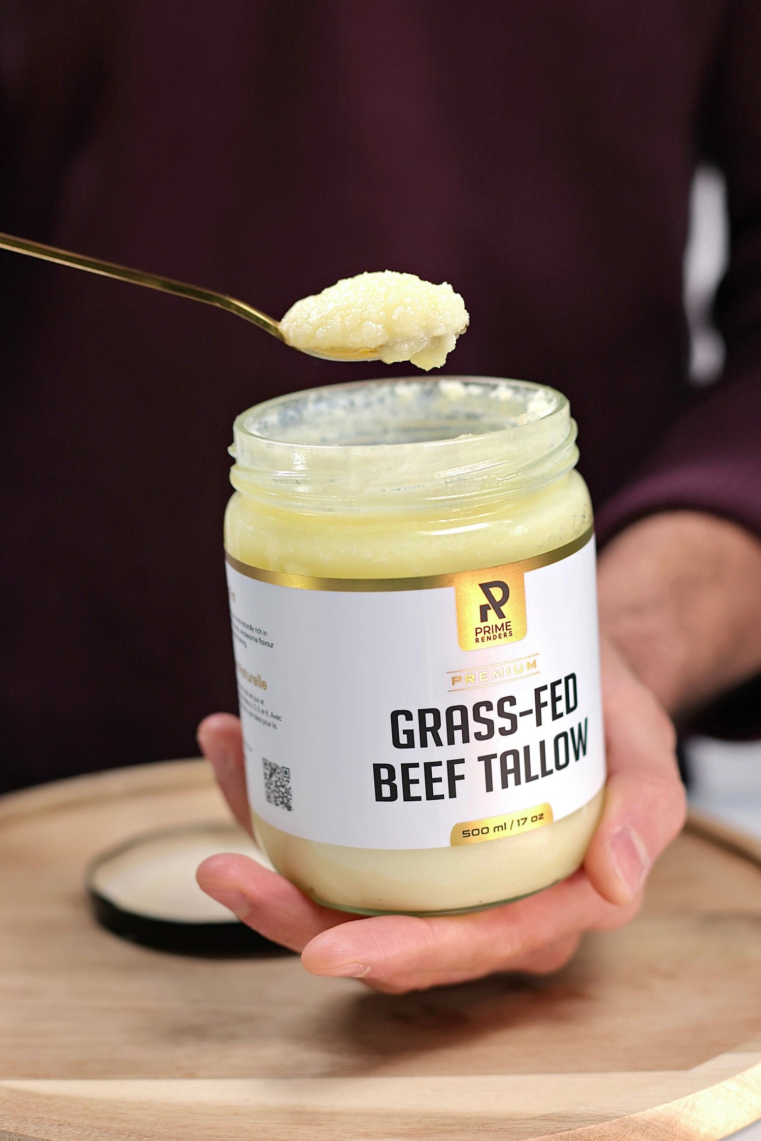 Jar of grass-fed beef tallow with a spoonful being lifted, held by a person.