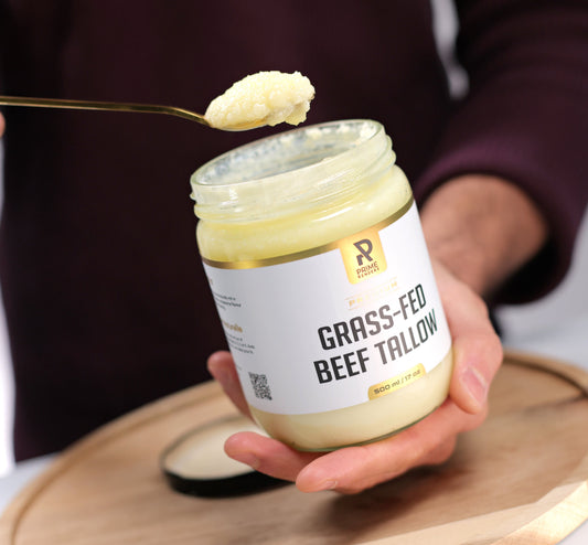 Person holding a jar of grass-fed beef tallow with a spoonful above it on a wooden board.