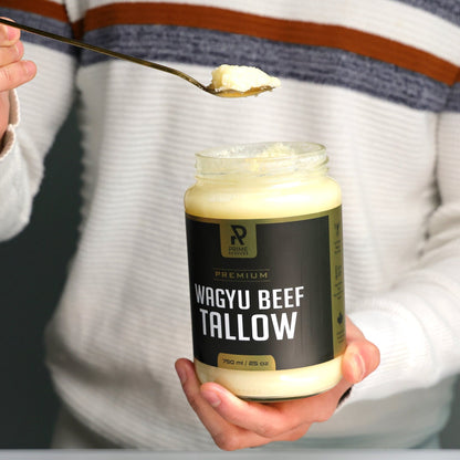 Person holding a jar of Wagyu Beef Tallow with a spoonful above it on a cutting board.